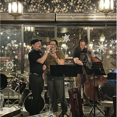 One person sings another holds a phone showing him the lyrics. A third musician plays stand up bass during the jass jam.
